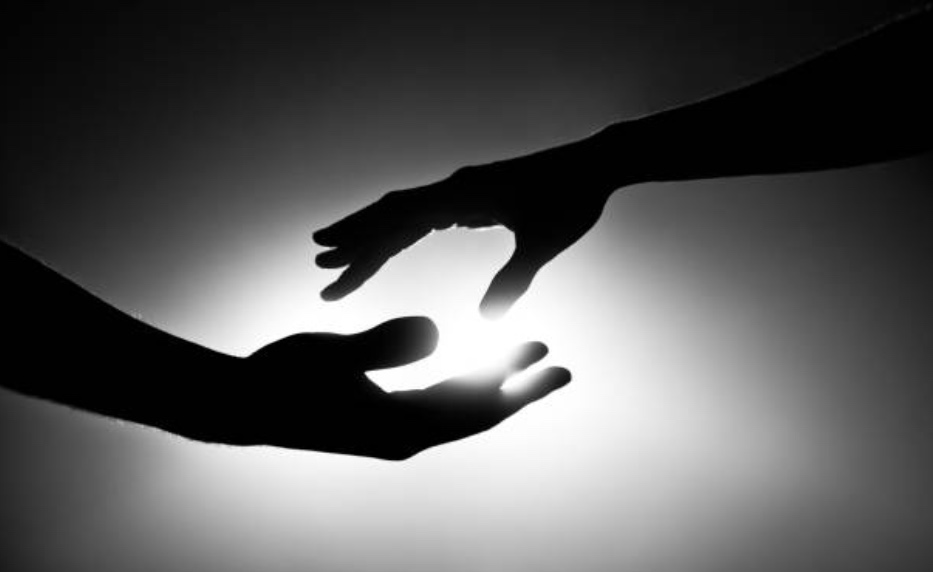 Two hands in silhouette reaching toward each other, a warm light glowing in the gap between their fingertips
